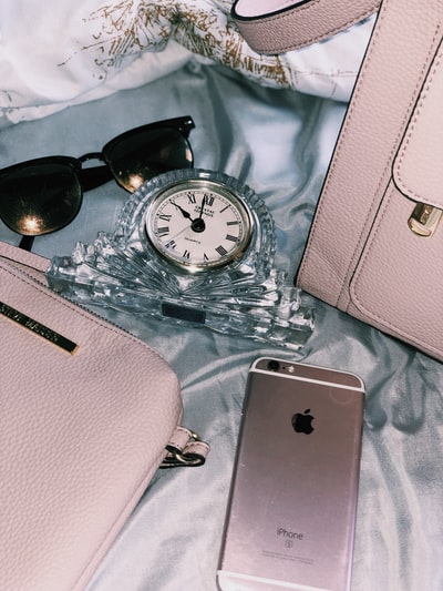 黄金iPhone 6 s附近的黑框太阳镜,粉红色的皮包,和清晰的模拟时钟
